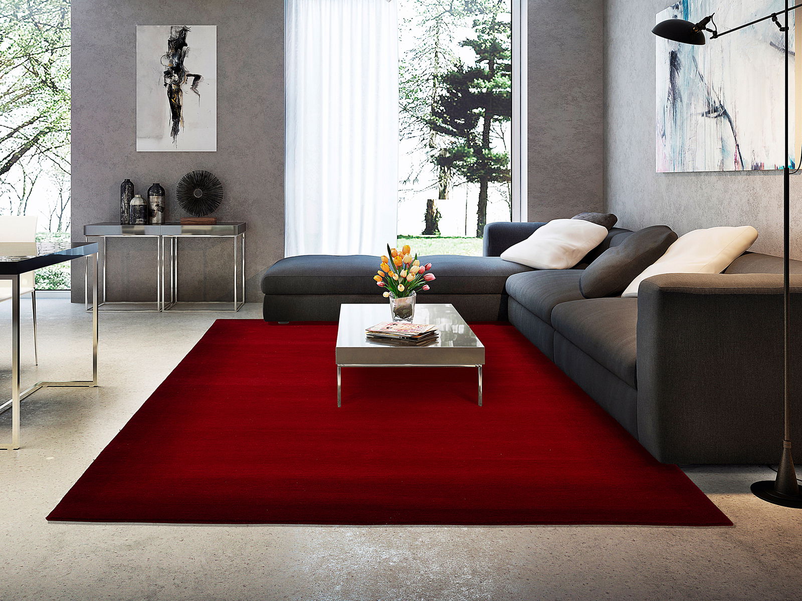 Moderner Wohnraum mit einem großen, roten Wollteppich im Vordergrund, der unter einem Couchtisch und einer grauen Eckcouch liegt. Die Perspektive zeigt den Teppich von oben in einem stilvoll eingerichteten Wohnzimmer.