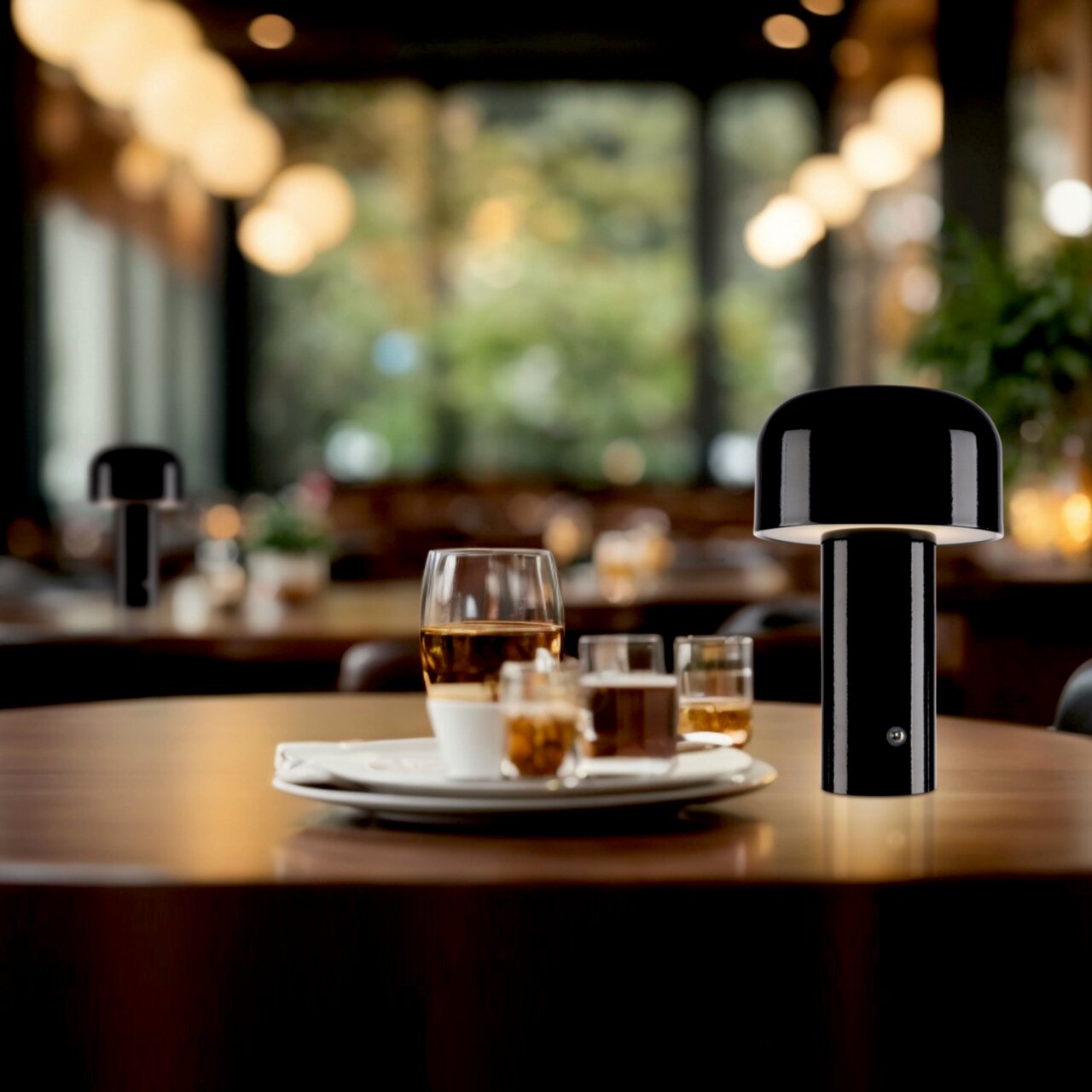 Schwarze Akku-Tischleuchte AGNES auf einem gedeckten Tisch in einem gemütlichen Restaurant, seitliche Perspektive.