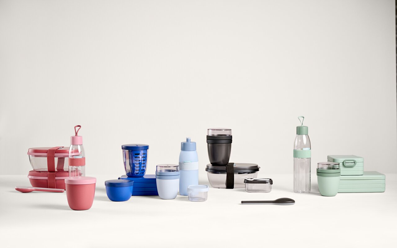 Verschiedene bunte Küchen- und Aufbewahrungsbehälter, darunter Flaschen, Dosen und Boxen, auf einem Tisch aus seitlicher Perspektive.