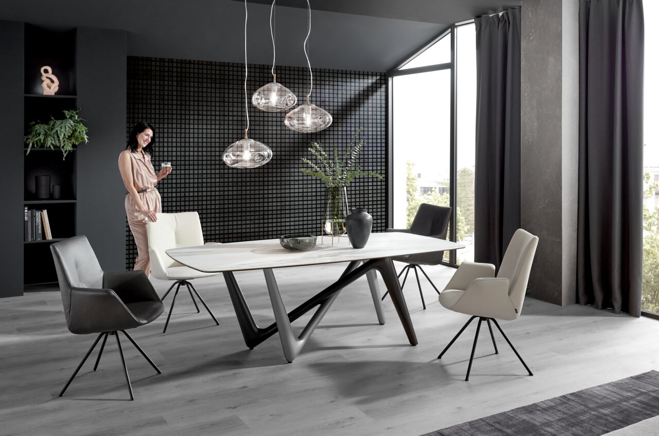 Moderne eethoek met een stijlvolle tafel en vier elegante stoelen in een lichte ruimte met grote ramen, zijaanzicht.