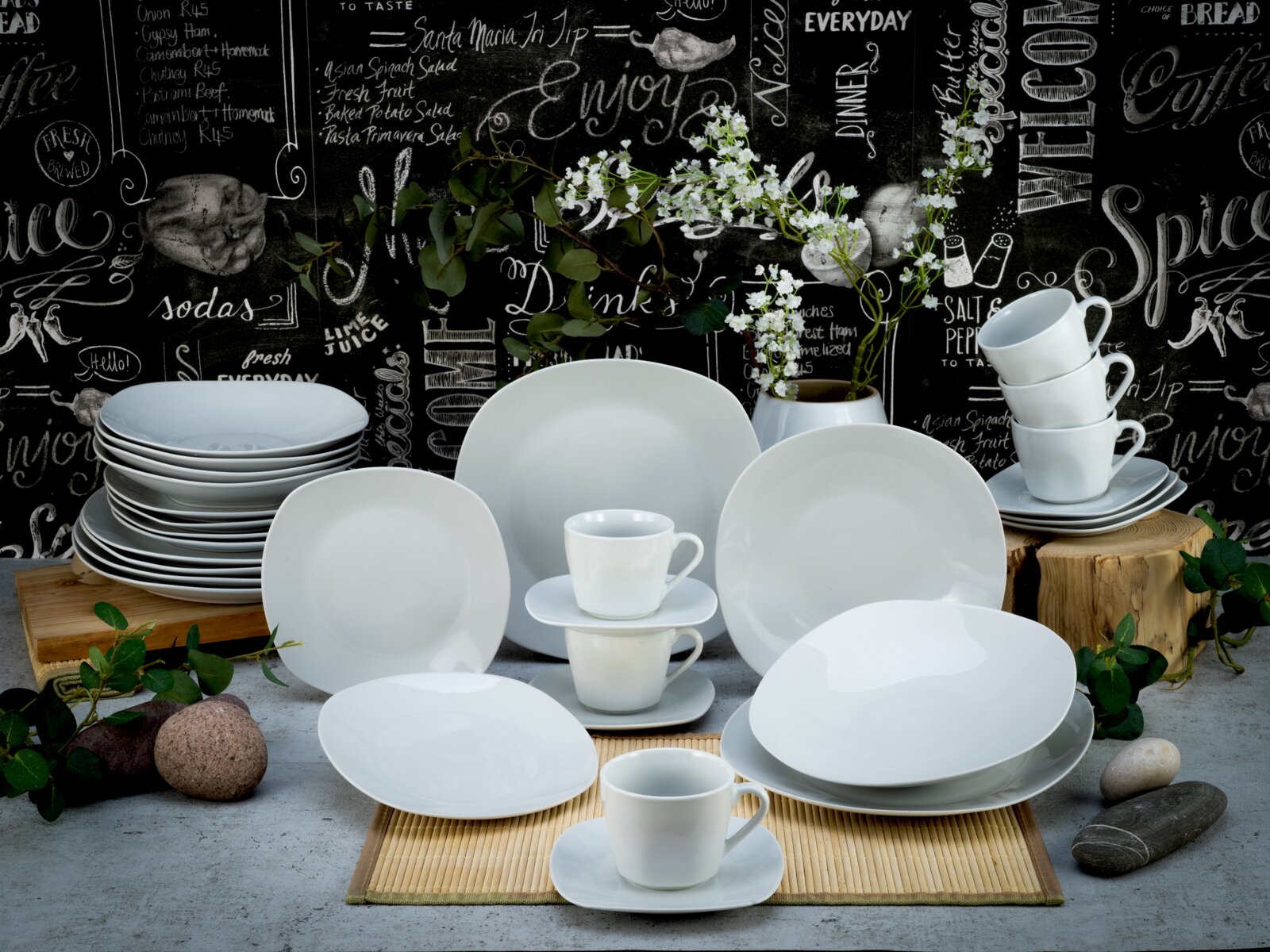 Creatable Kombiservice 30-tlg SQUARE Weißes Porzellan-Tafelservice mit Tellern, Schalen und gestapelten Tassen dekorativ arrangiert vor Tafelhintergrund, fotografiert in frontaler Perspektive auf Tischhöhe.