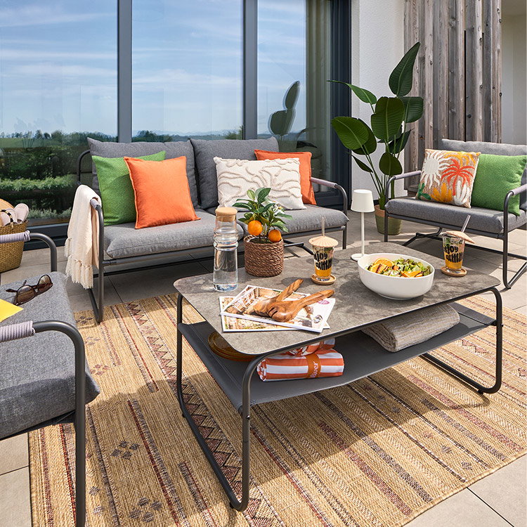 Gemütliche Terrasse mit Sofa, Sesseln, Tisch, bunten Kissen und Blick ins Grüne.
