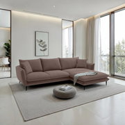 Moderne L-vormige hoekbank in taupe met een poef aan de rechterkant en zwarte metalen poten in een lichte woonkamer, vooraanzicht licht van links.