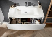 Modernes weißes Bad-Waschbecken mit integriertem Waschtisch und geöffneter Schublade mit Organizer und Pflegeartikeln, Ansicht leicht von oben/Frontperspektive.