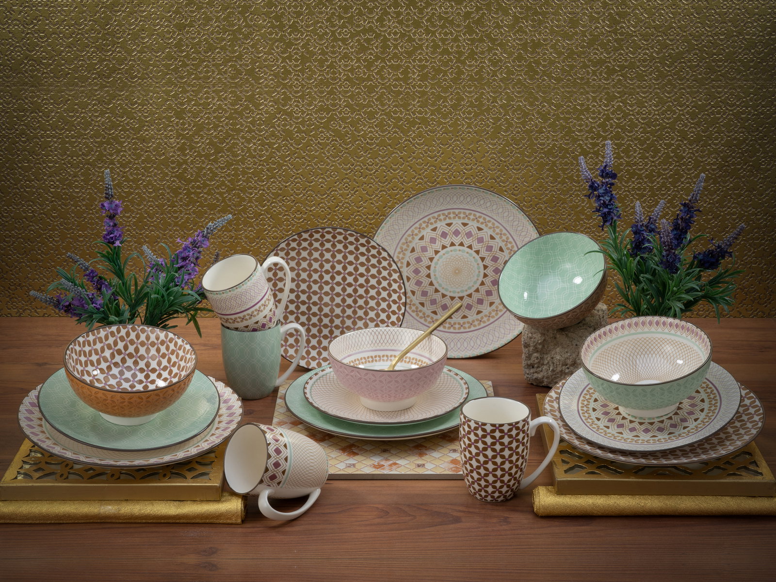 Creatable Kombiservice 16-tlg MANDALA Kombiservice 16-tlg mit bunten geometrischen Mustern, bestehend aus Tellern, Schalen und Tassen, auf einem Holztisch mit dekorativen Pflanzen im Hintergrund, aus der Vorderansicht fotografiert.