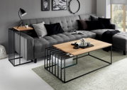 Woonkameropstelling met een moderne salontafel met een lichtgekleurd houten blad en een zwart metalen onderstel met opbergruimte, met daarvoor een grijze hoekbank; perspectief: licht zijdelings vooraanzicht vanaf ooghoogte.