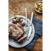Het Nuova-steakbestek op een rustieke houten tafel, naast een bord met een sappige steak en groenten, gefotografeerd vanuit vogelperspectief.