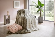 Gezellige bontdekens in verschillende kleuren, gedrapeerd over een fauteuil in een moderne woonkamer met uitzicht op de tuin.