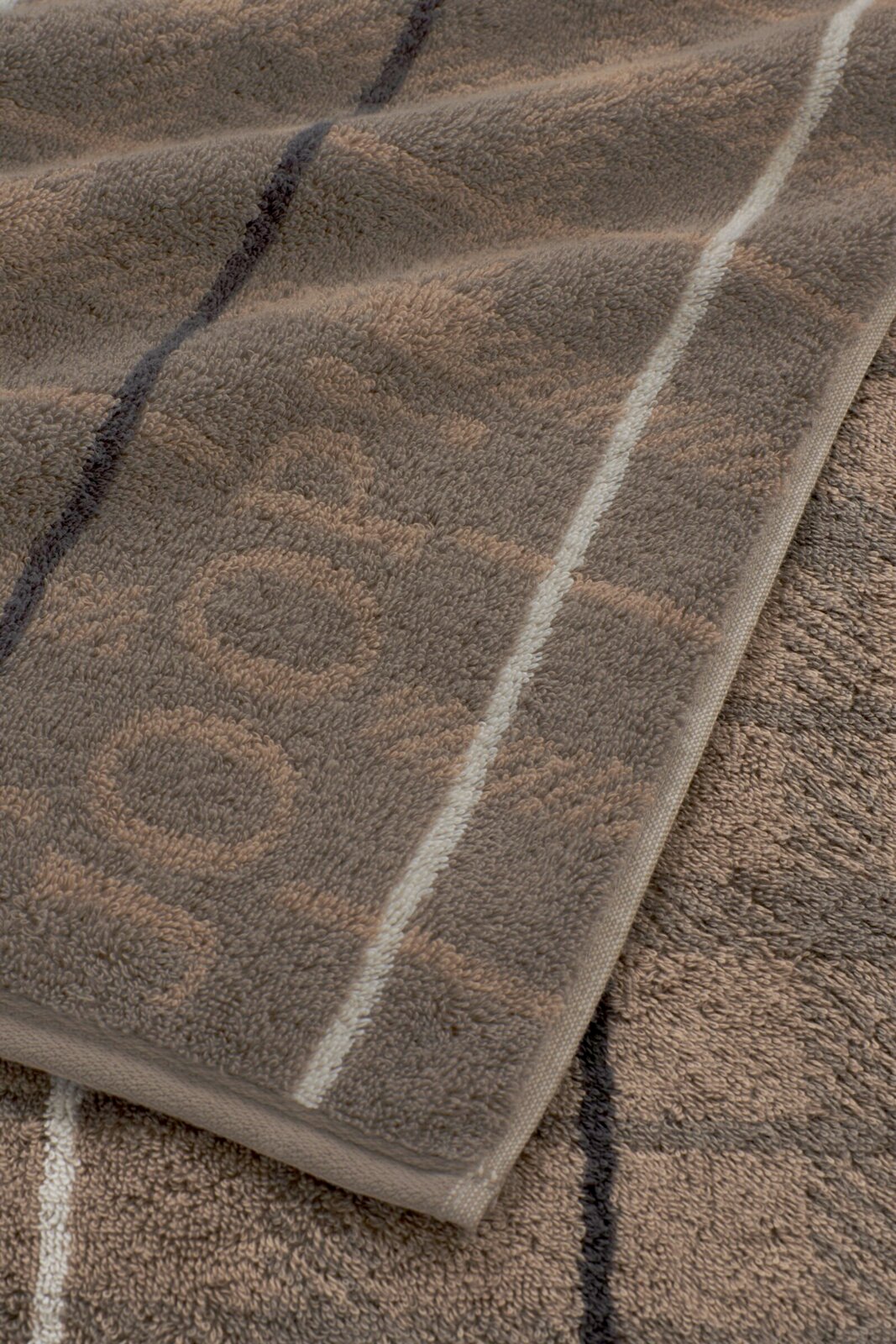 Nahaufnahme in leichter Schrägansicht von einem weichen Frottee-Handtuch in Taupe mit hellen und dunklen Streifen sowie gewebter Bordüre am Rand