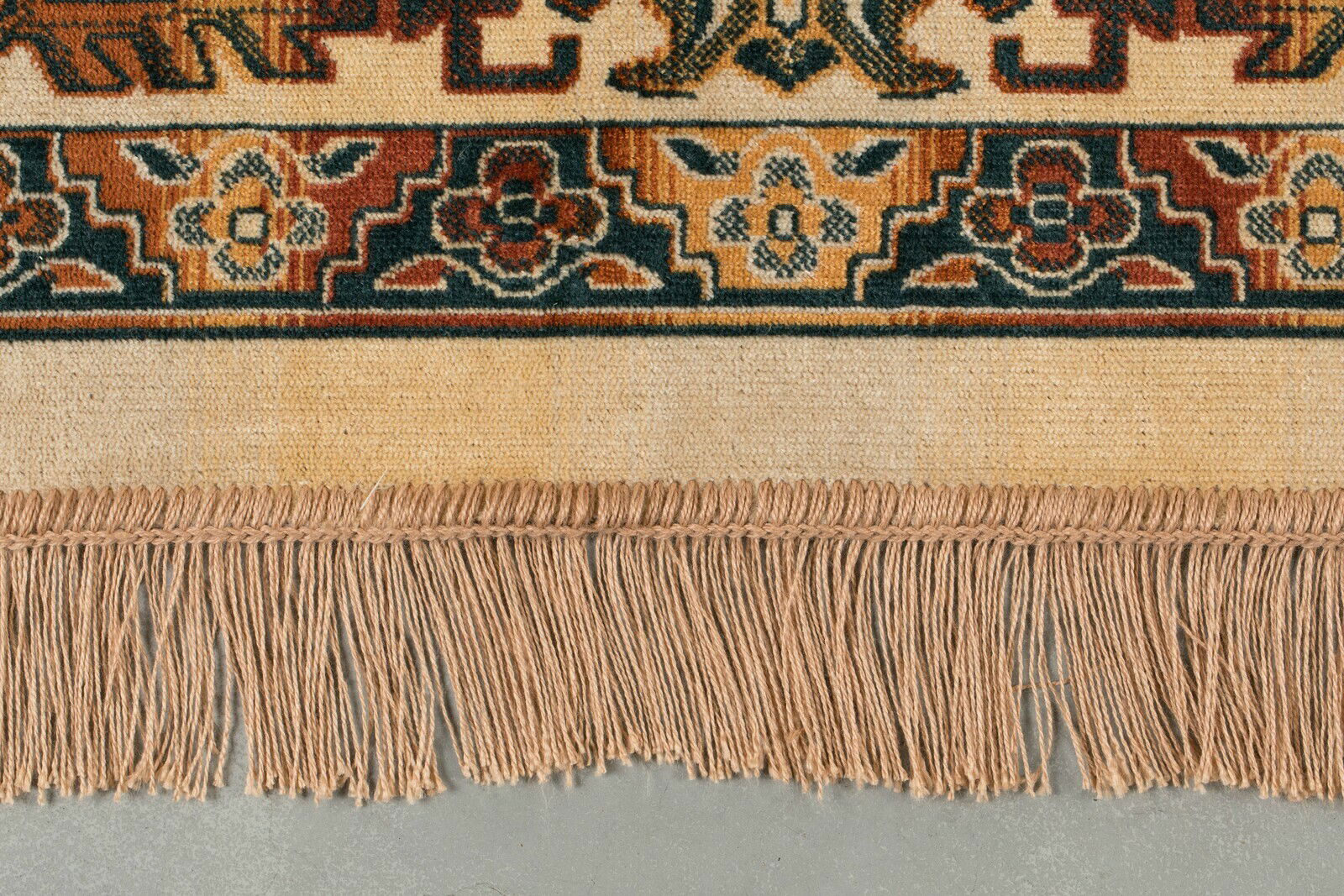 Nahaufnahme eines Teppichs mit buntem, traditionellem Muster und Fransen am Rand, von oben betrachtet.