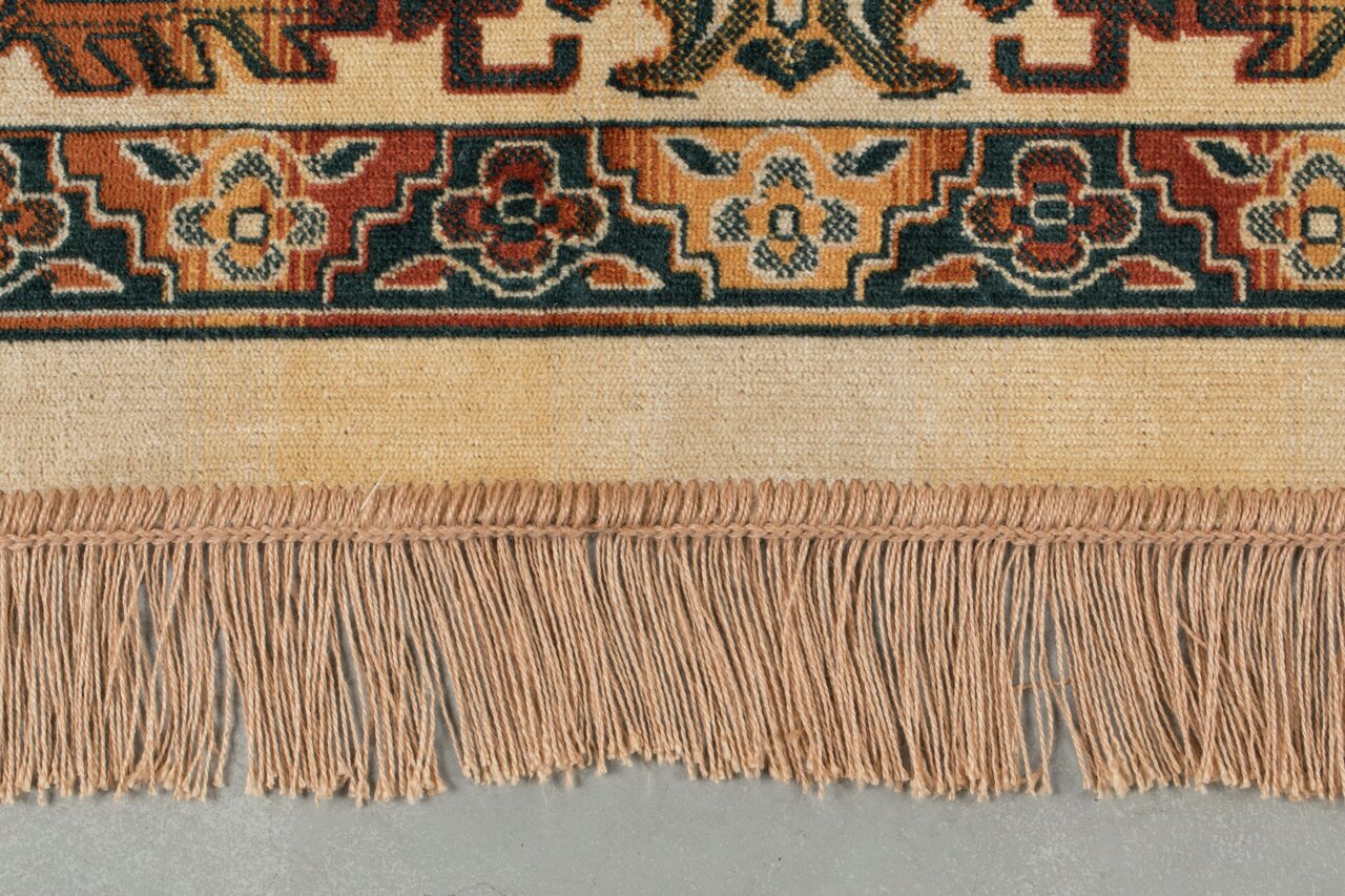 Nahaufnahme eines Teppichs mit buntem, traditionellem Muster und Fransen am Rand, von oben betrachtet.