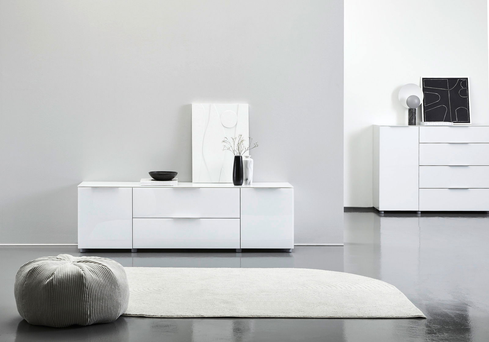 Modernes weißes Sideboard in einem minimalistischen Raum, frontal betrachtet, mit Dekorationen wie einer Vase und einem Kunstwerk darauf.