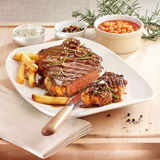 Ein saftiges Steak mit Pommes frites und Rosmarin auf einem weißen Teller, begleitet von Beilagen wie Bohnen und Gewürzen, aus der Vogelperspektive fotografiert.