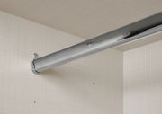Nahaufnahme einer stabilen, silbernen Kleiderstange in einem Schwebetürenschrank, montiert an einer hellen, strukturierten Innenwand.