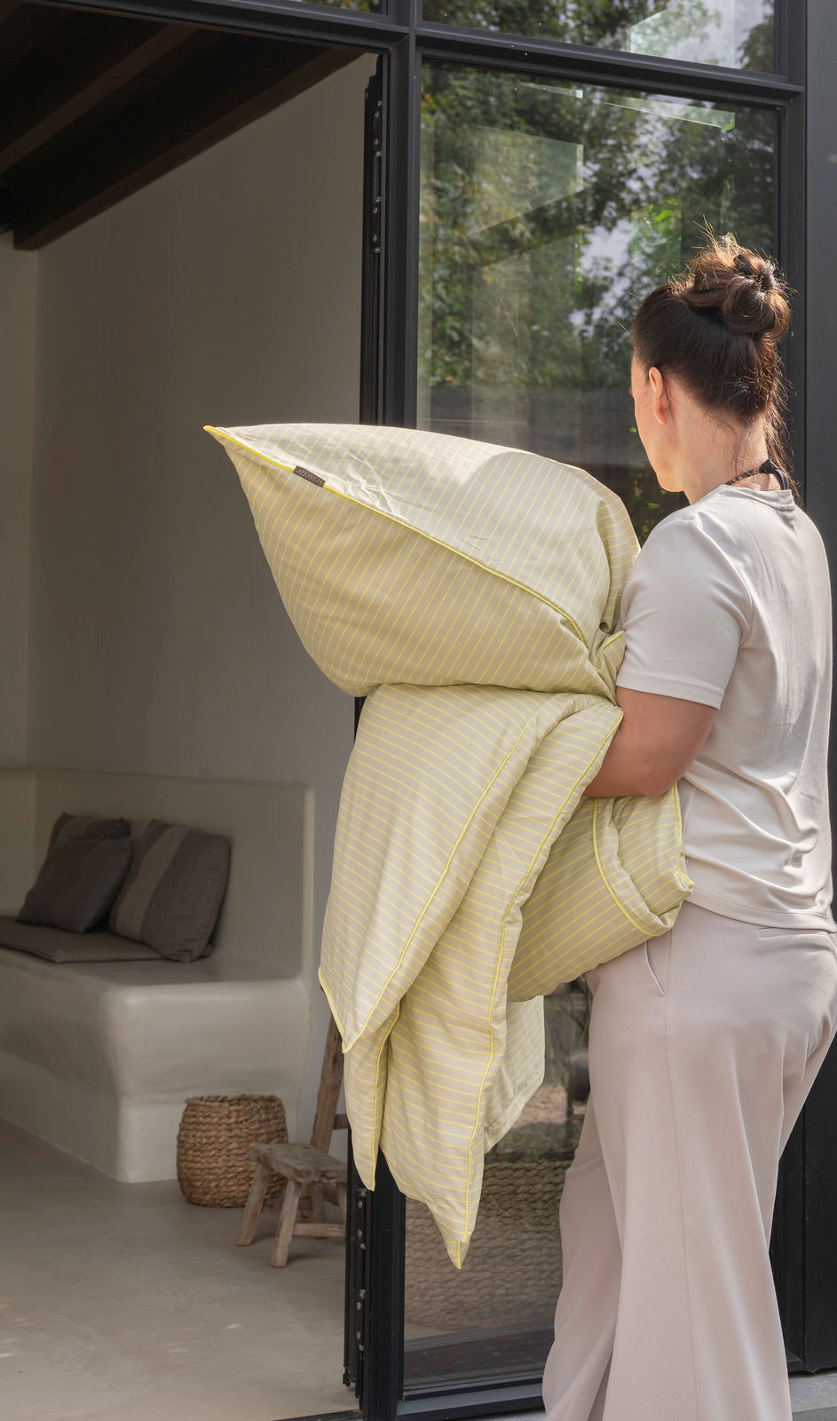Person trägt gelb gestreifte Bettwäsche in einem modernen, lichtdurchfluteten Raum.