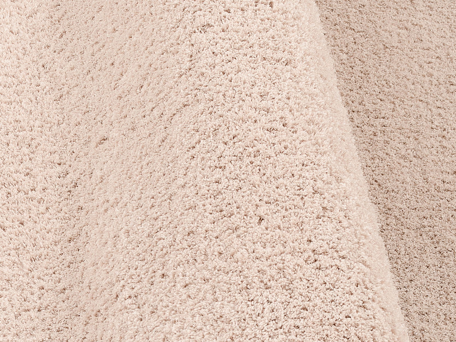 Nahaufnahme eines beigen, flauschigen Teppichs mit weicher Textur, perspektivisch von der Seite aufgenommen.