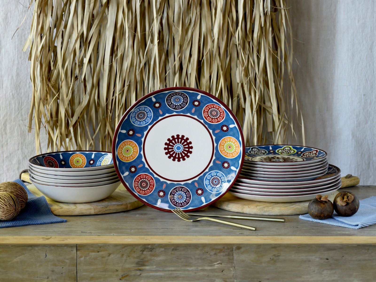 Creatable Tellerset 18-tlg SUMAYA Bunt gemustertes Keramikgeschirr-Set mit Teller und Schalen in Blau, Rot und Orange, dekorativ auf Holztisch arrangiert; Perspektive: Frontalansicht mit zentralem Teller von vorne.