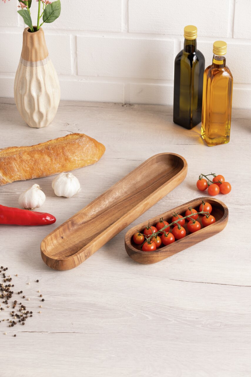 Houten bakje voor baguettes in rechthoekige vorm, gefotografeerd van bovenaf, omringd door baguettes, knoflook, paprika’s, tomaten en olieflesjes.
