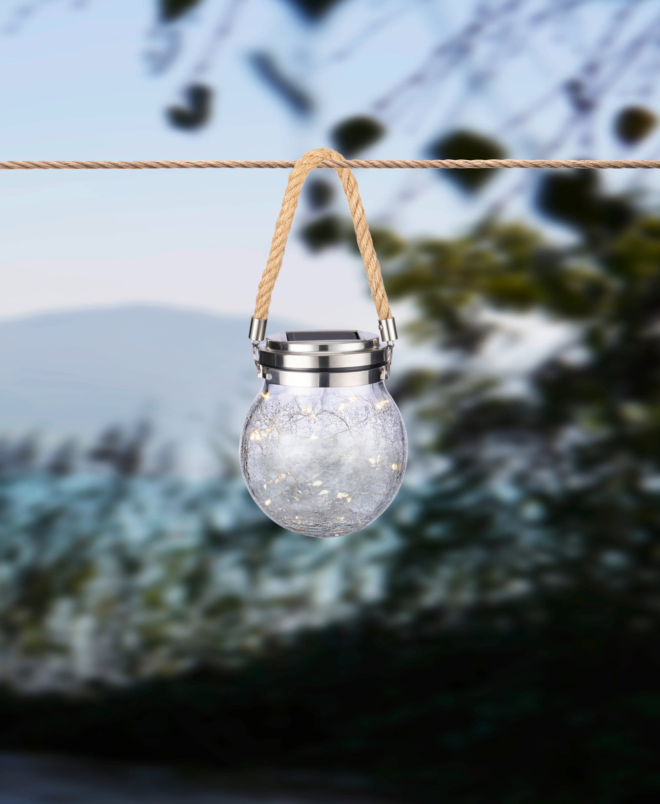 Ambia Garden Zonne-lamp Solarleuchte in Form eines Glases mit Seilaufhängung, von vorne fotografiert, im Freien aufgehängt.