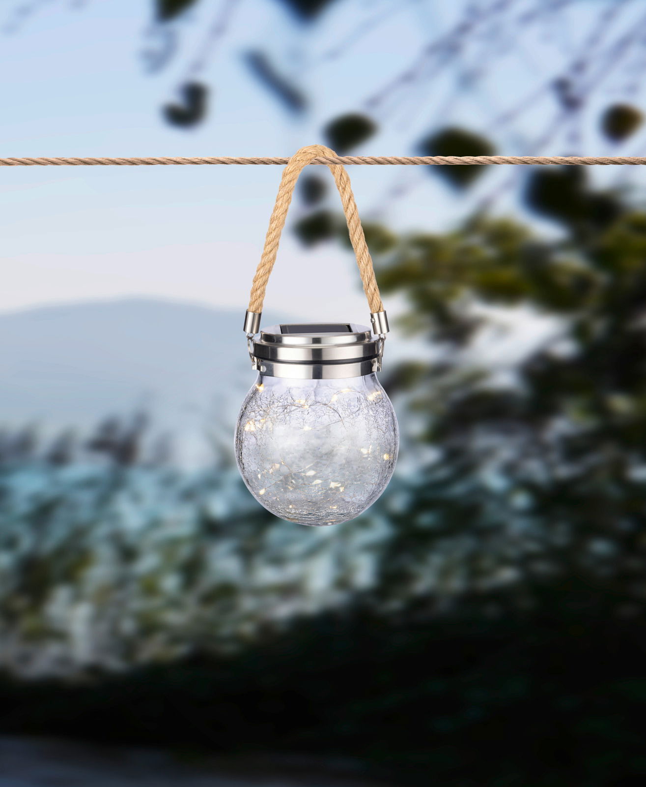 Solarleuchte in Form eines Glases mit Seilaufhängung, von vorne fotografiert, im Freien aufgehängt.