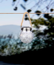 Zonne-lamp in de vorm van een glas met een touwophanging, van voren gefotografeerd, buiten opgehangen.