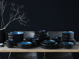 Kombiservice 30-tlg. Blue in eleganter schwarzer und blauer Keramik, auf einem Tisch arrangiert, seitliche Perspektive.