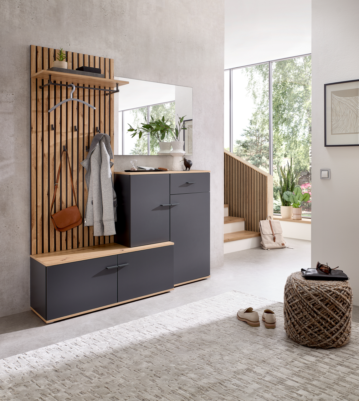 Moderne Kompaktgarderobe in einem hellen Raum, bestehend aus einer Holzpaneelwand mit Haken, einem Spiegel und grauen Schränken. Perspektive von vorne.