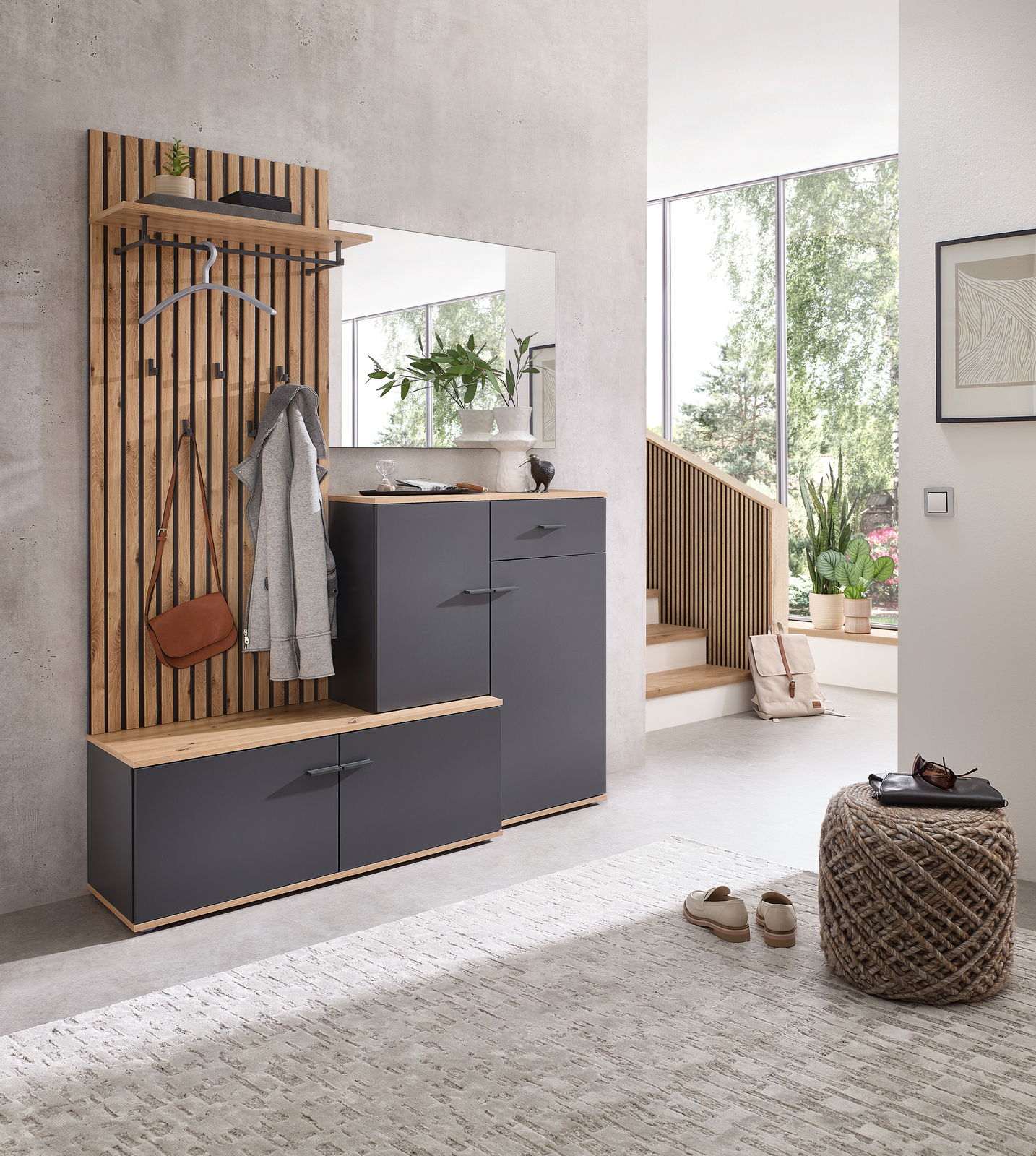 Moderne Kompaktgarderobe in einem hellen Raum, bestehend aus einer Holzpaneelwand mit Haken, einem Spiegel und grauen Schränken. Perspektive von vorne.
