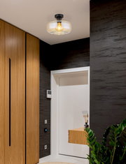 Moderne Deckenleuchte mit Glasabdeckung und sichtbarer Glühbirne, von unten betrachtet in einem stilvollen Flur mit Holzelementen.