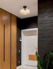 Moderne Deckenleuchte mit Glasabdeckung und sichtbarer Glühbirne, von unten betrachtet in einem stilvollen Flur mit Holzelementen.