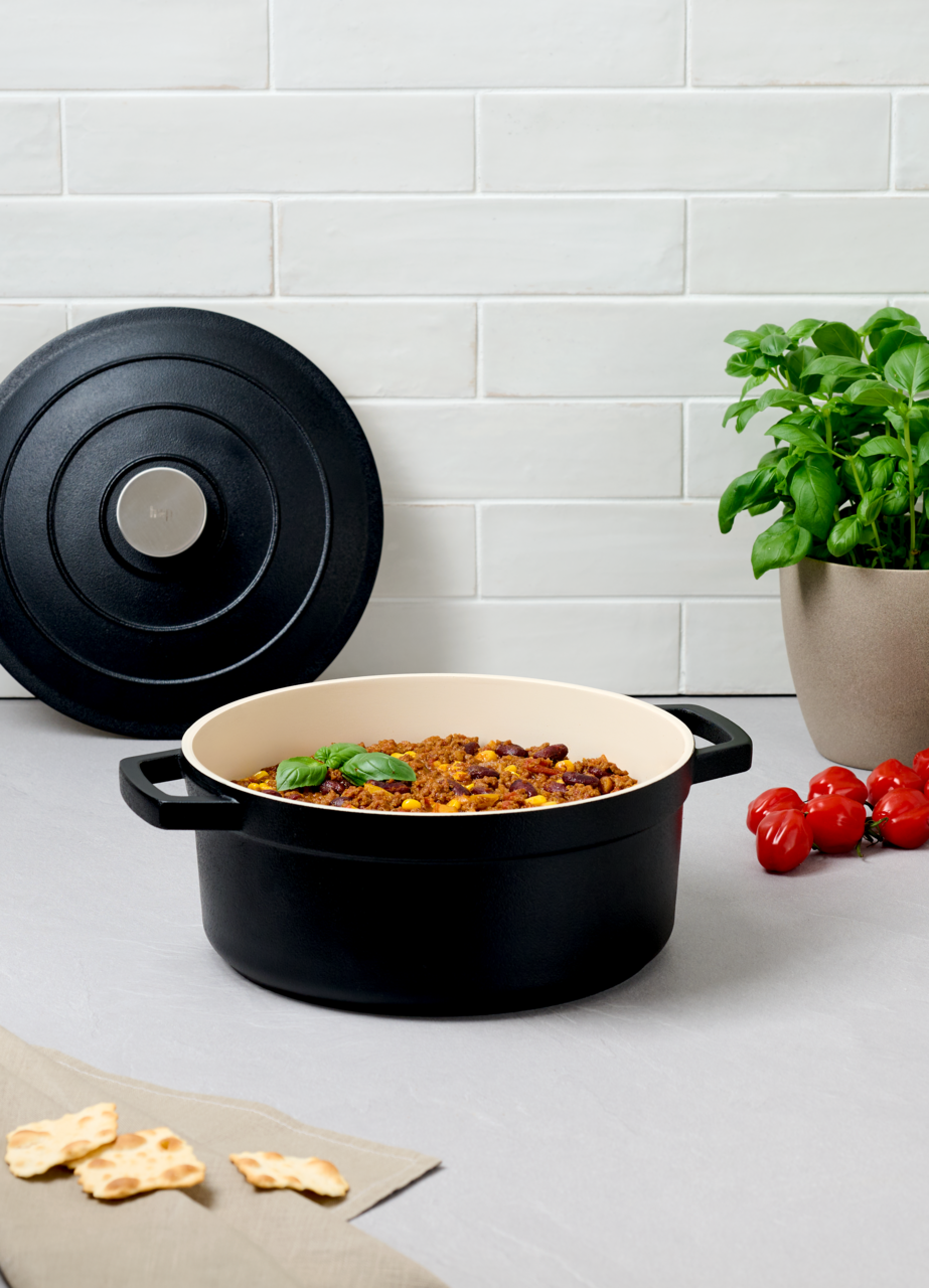 Homeware Kochtopf 24cm Schwarzer Kochtopf 24cm mit Deckel, gefüllt mit einem Gericht, auf einer Küchenarbeitsplatte, seitliche Perspektive.