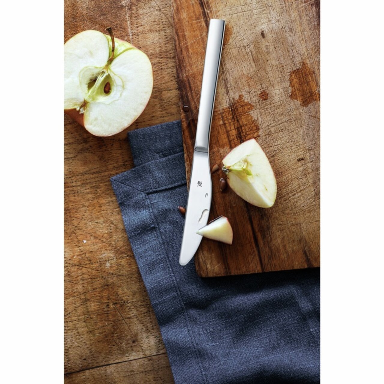 Obstmesser auf einem Holzbrett mit geschnittenem Apfel, von oben betrachtet