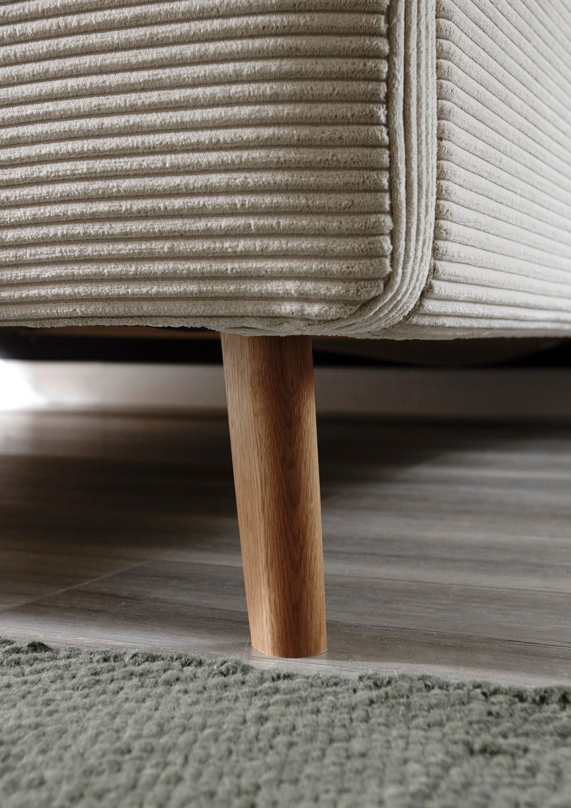 Nahaufnahme eines Polsterbettgestells mit Holzbein, seitliche Perspektive