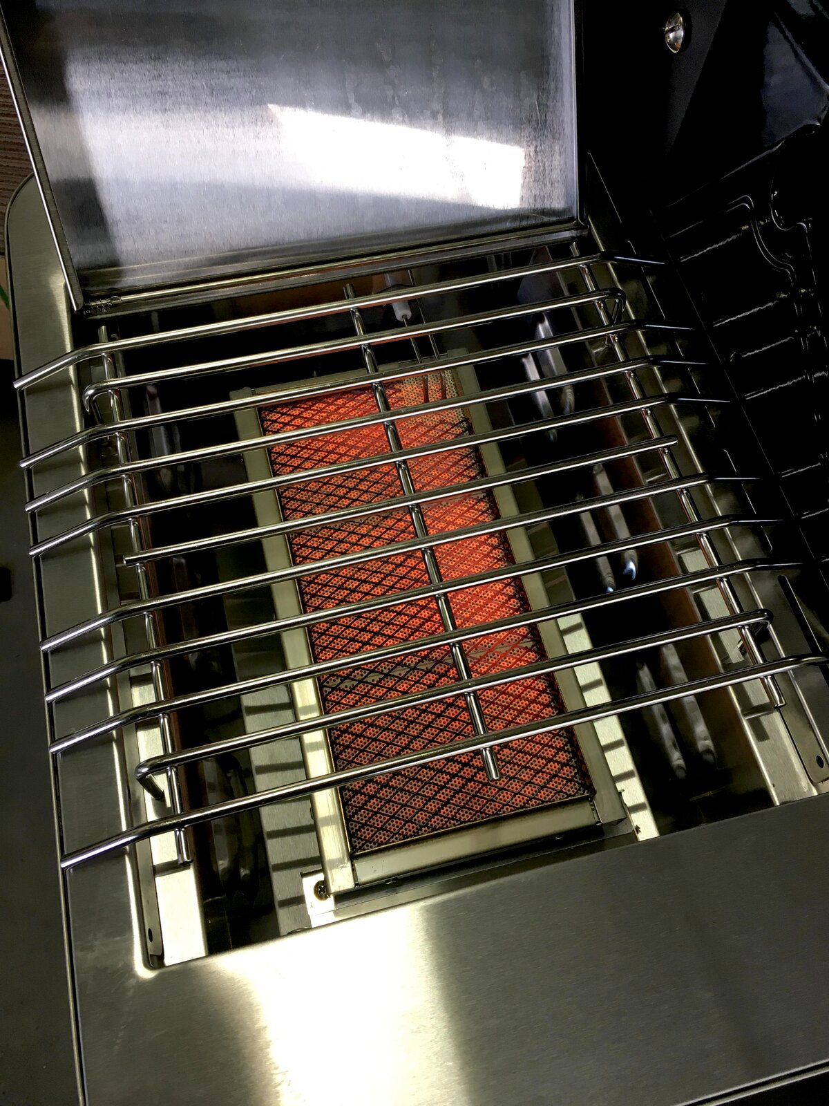 Edelstahl-Gasgrill mit geöffnetem Deckel, Blick von oben in den Garraum auf den Grillrost und den glühenden Keramikbrenner