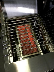 Edelstahl-Gasgrill mit geöffnetem Deckel, Blick von oben in den Garraum auf den Grillrost und den glühenden Keramikbrenner