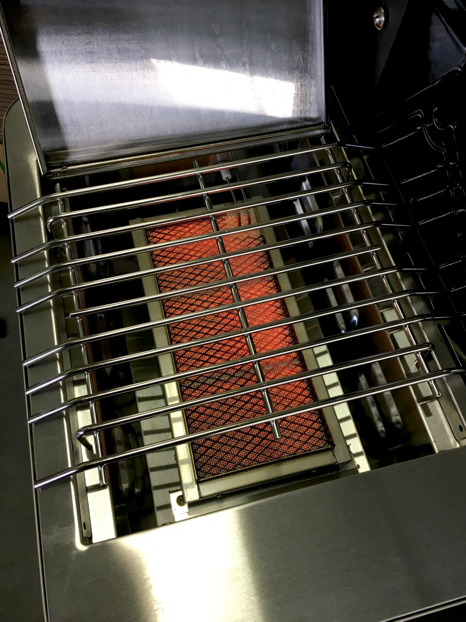 Edelstahl-Gasgrill mit geöffnetem Deckel, Blick von oben in den Garraum auf den Grillrost und den glühenden Keramikbrenner
