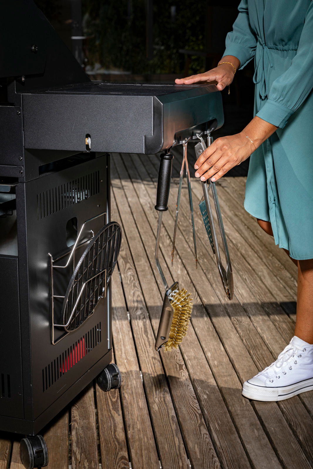 Nahaufnahme eines Gasgrills mit Zubehör, darunter Grillzange und Grillbürste, von der Seite betrachtet.