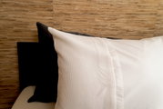 Nahaufnahme von Bettwäsche in Weiß mit strukturiertem Muster, auf einem Bett mit Holzwand im Hintergrund.