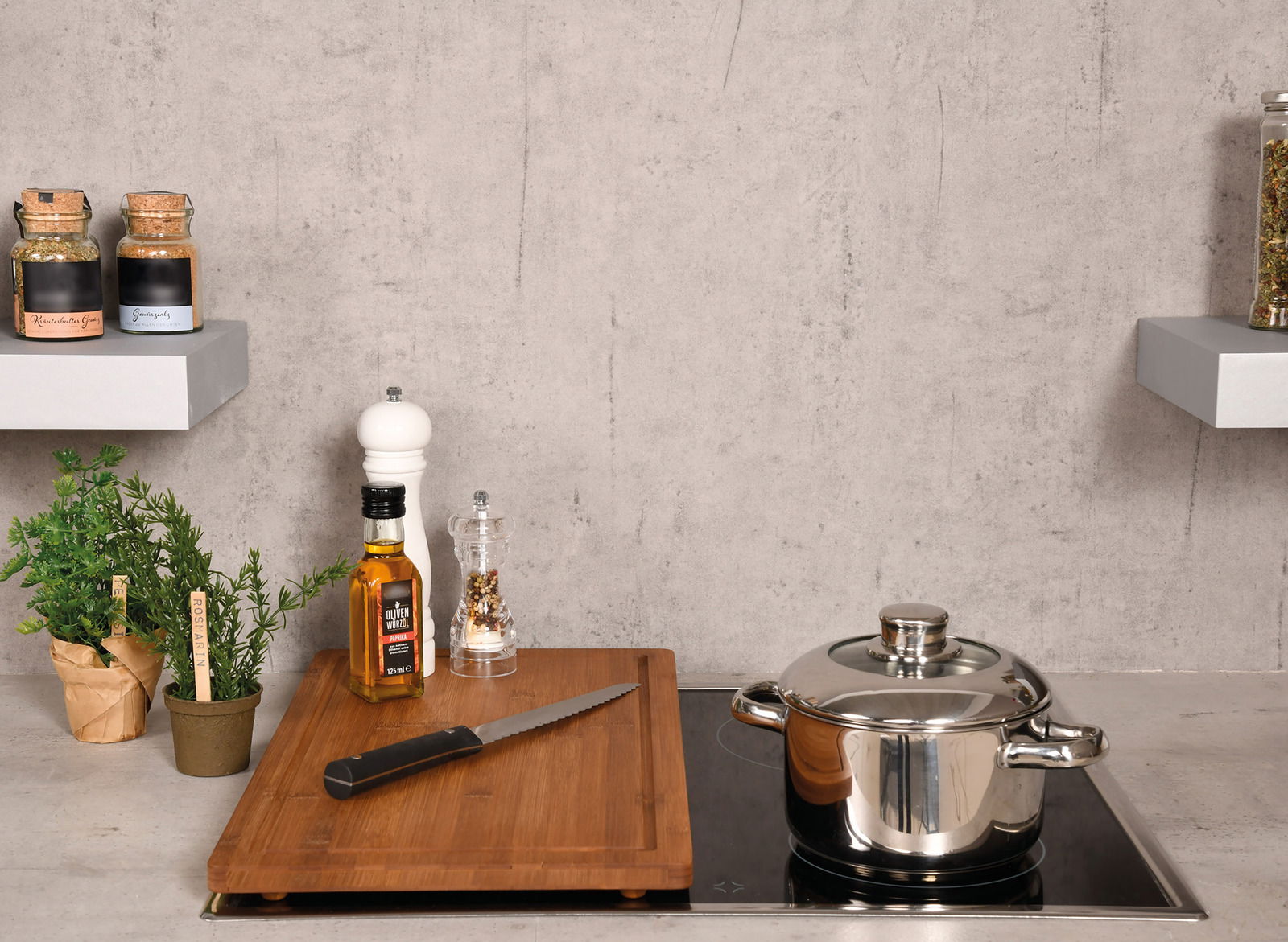 Schneide- und Abdeckplatte aus Holz auf einem Herd, mit einem Messer, einer Flasche Olivenöl und Gewürzen, aus der Perspektive von vorne.