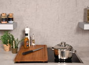 Schneide- und Abdeckplatte aus Holz auf einem Herd, mit einem Messer, einer Flasche Olivenöl und Gewürzen, aus der Perspektive von vorne.