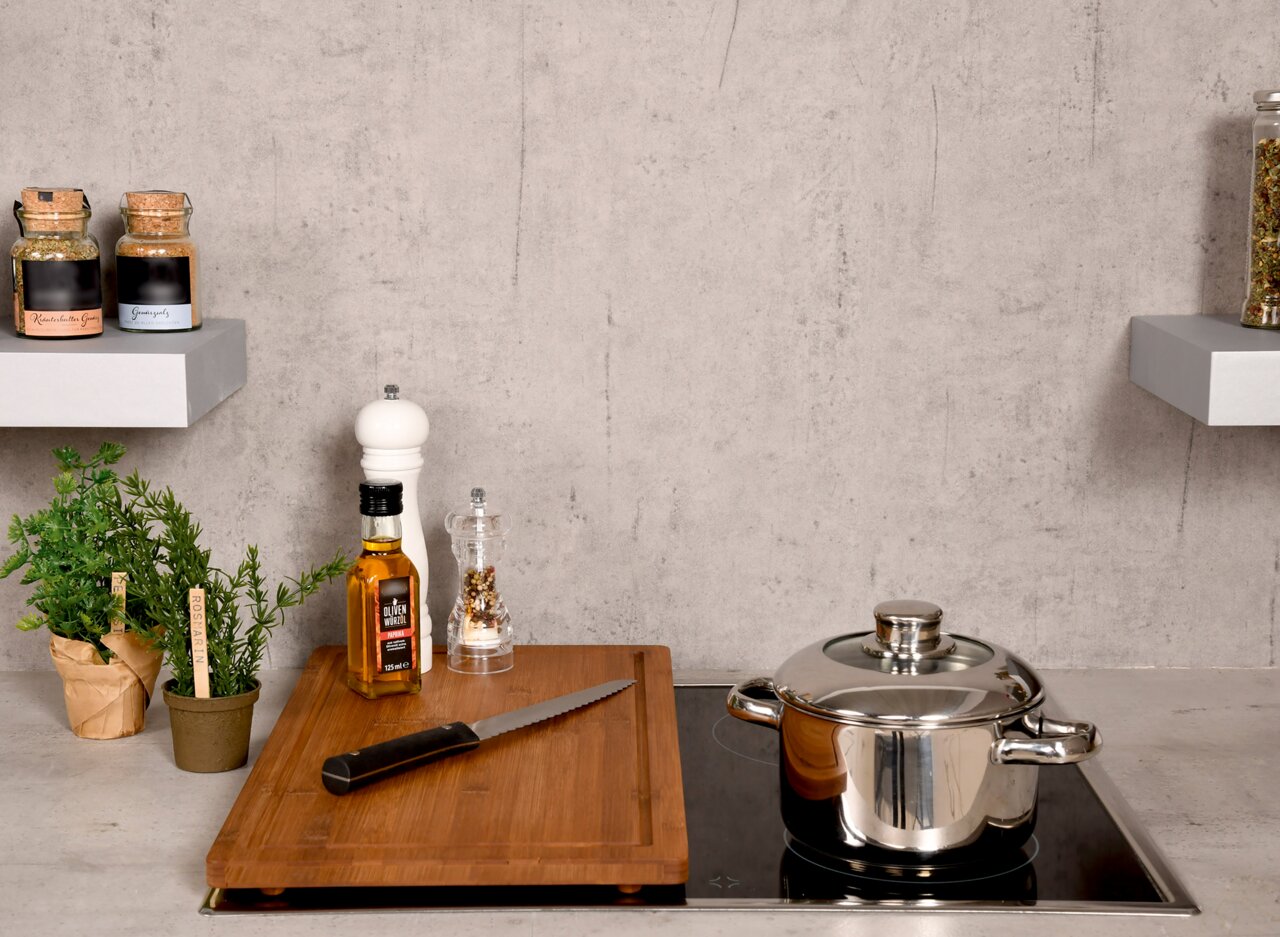 Kesper Schneide- und Abdeckplatte Schneide- und Abdeckplatte aus Holz auf einem Herd, mit einem Messer, einer Flasche Olivenöl und Gewürzen, aus der Perspektive von vorne.