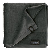 Dunkelgraues Frottierset, bestehend aus einem gefalteten Handtuch mit sichtbarem Etikett, aus der Vogelperspektive fotografiert.