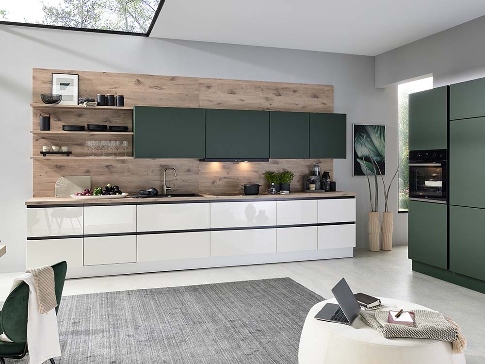Moderne Küche mit grünen und weißen Schränken, Holzoptik, offenen Regalen und hellem Wohnbereich.