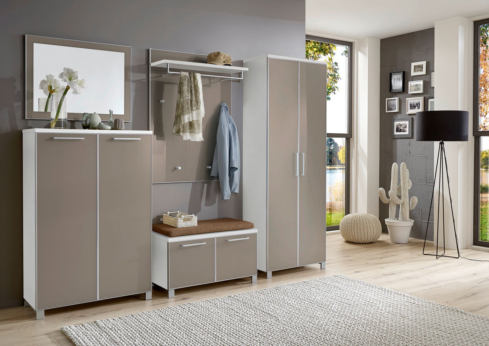 Modernes Garderoben-Set in Beige und Weiß, bestehend aus mehreren Schränken und einer Sitzbank, in einem hellen Raum mit großen Fenstern, aus der Perspektive von vorne betrachtet.