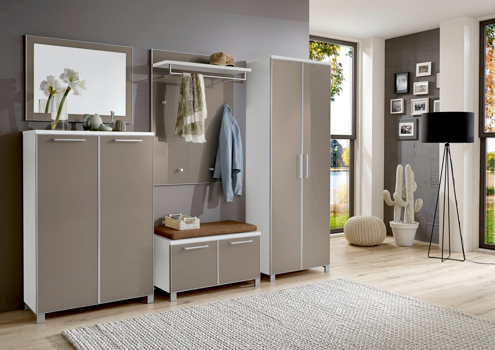 Modernes Garderoben-Set in Beige und Weiß, bestehend aus mehreren Schränken und einer Sitzbank, in einem hellen Raum mit großen Fenstern, aus der Perspektive von vorne betrachtet.