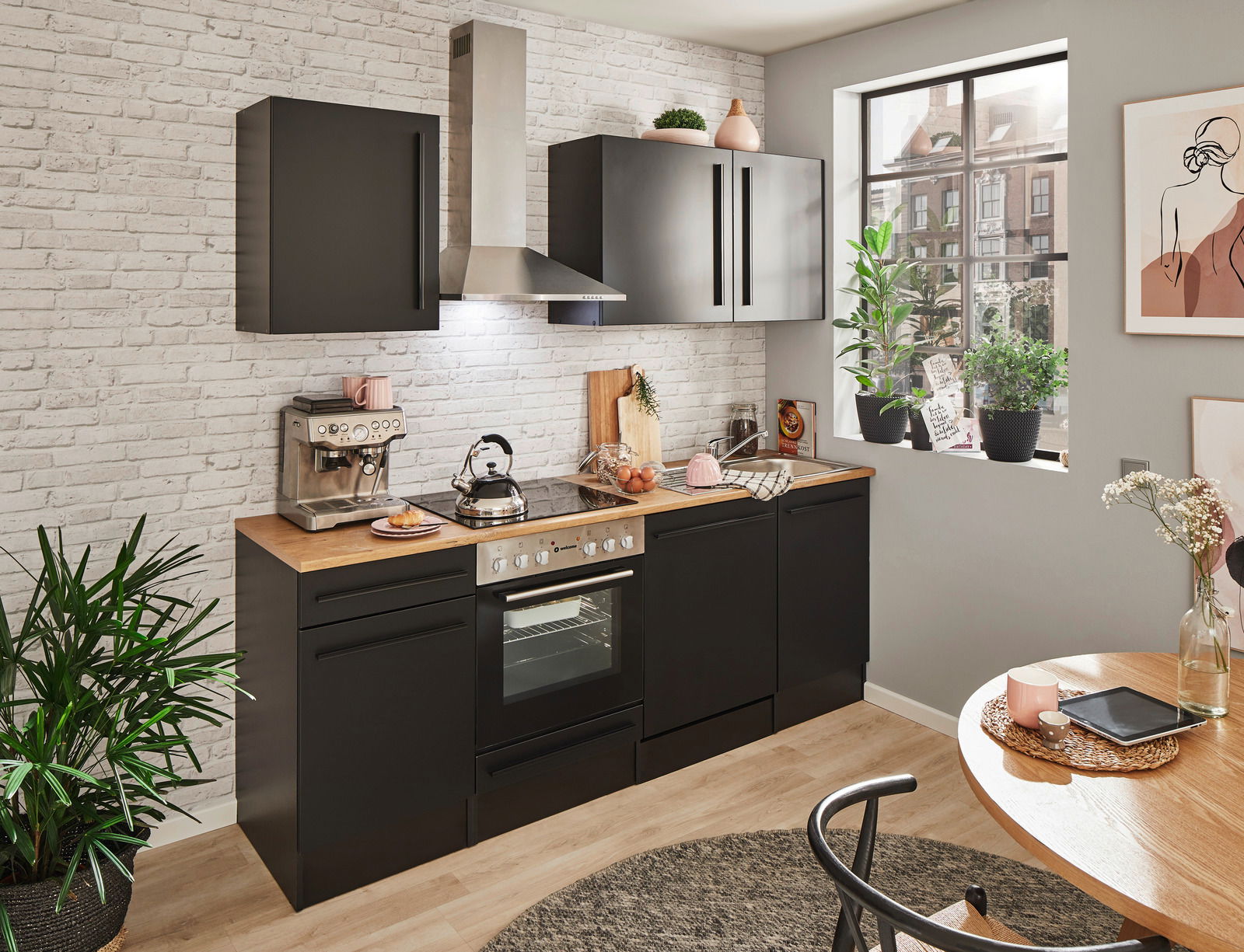 Moderne Küche in schwarzem Design mit Holzarbeitsplatte, ohne Elektrogeräte, aus der Perspektive eines hellen, gemütlichen Raumes mit Pflanzen und Dekorationen.