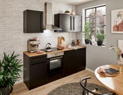 Moderne Küche in schwarzem Design mit Holzarbeitsplatte, ohne Elektrogeräte, aus der Perspektive eines hellen, gemütlichen Raumes mit Pflanzen und Dekorationen.