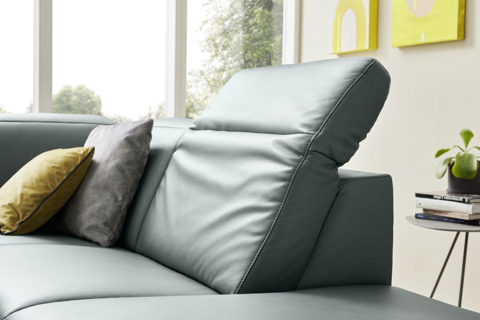 Nahaufnahme eines modernen Ecksofas in Lederoptik mit verstellbarer Kopfstütze und dekorativen Kissen, seitliche Perspektive.