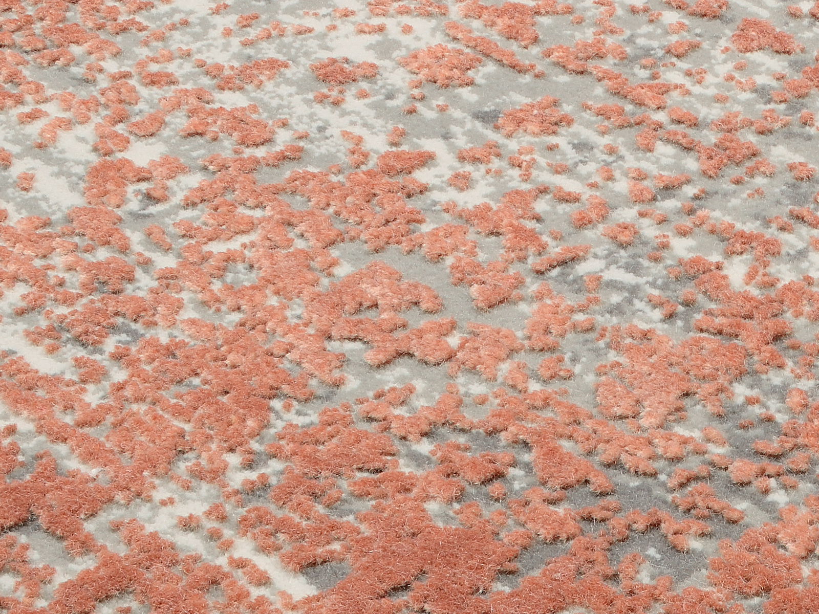 Nahaufnahme eines Designer-Teppichs mit abstraktem Muster in Rosa und Grau, aus schräger Perspektive aufgenommen.