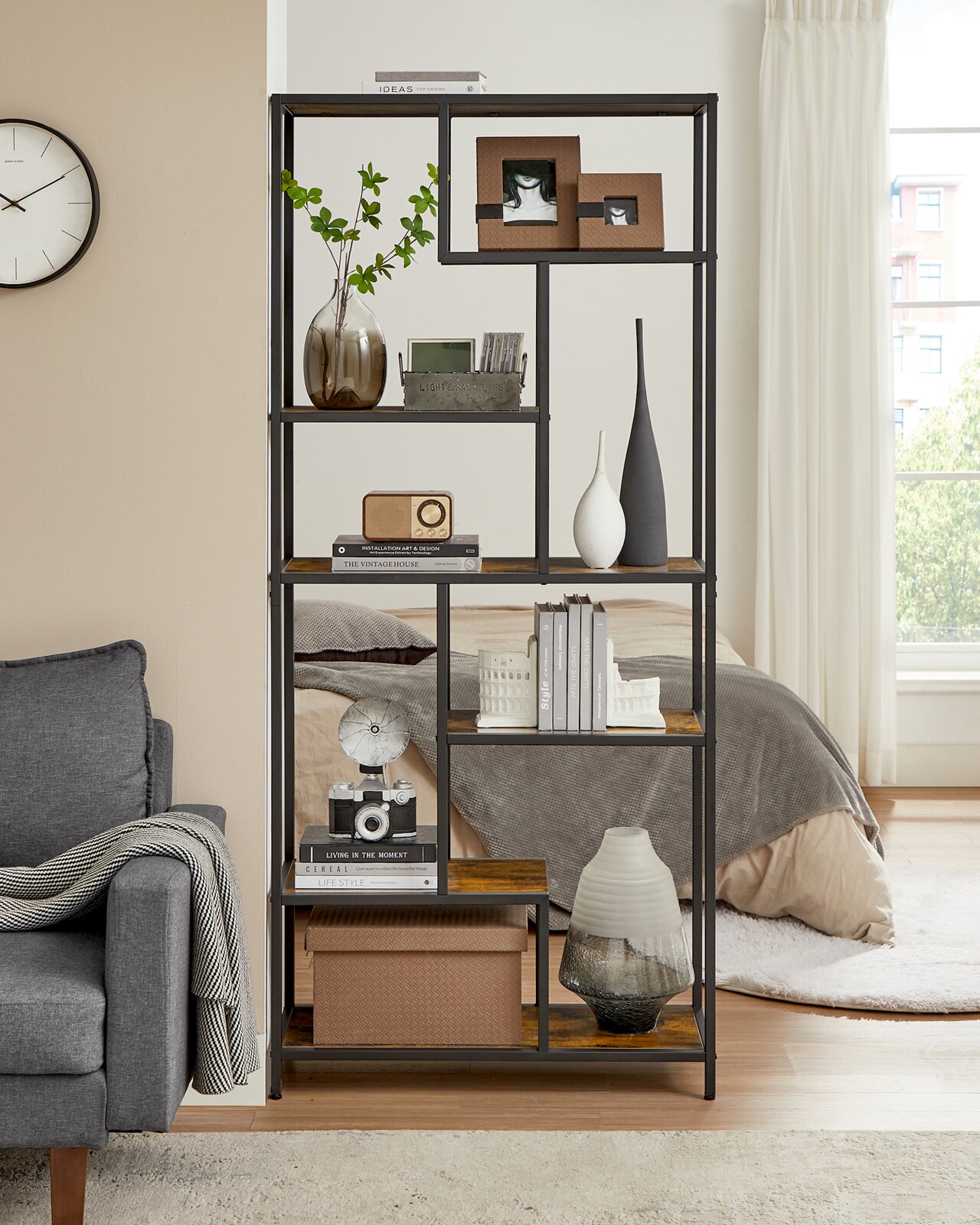 Frontale Ansicht eines hohen, offenen Regals im Industrial-Design mit schwarzem Metallrahmen und Holzböden, dekoriert mit Vasen, Büchern, Boxen und Bildern im Wohn-/Schlafzimmer neben einem Fenster.